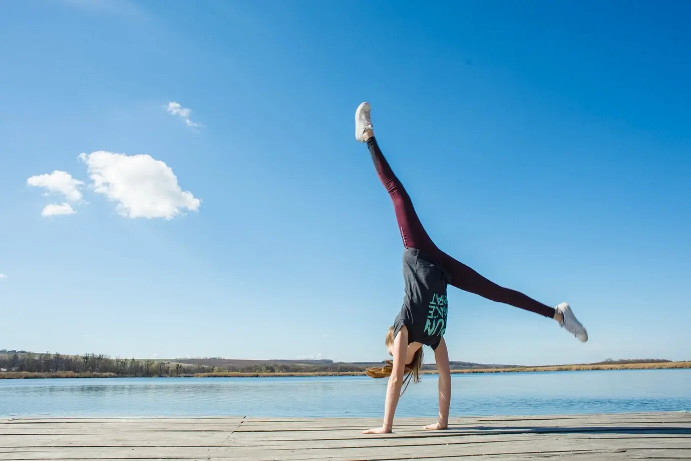 Подросток выполняет стойку на руках на пирсе.